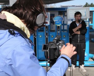 ein junger Mann vor Zapfsäulen an einer Tankstelle wird gefilmt