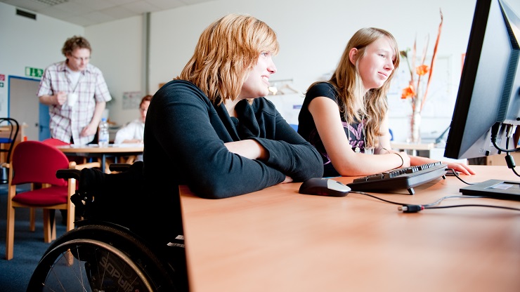 Zwei Mädchen vor dem Computer, ein Mädchen nutzt einen Rollstuhl