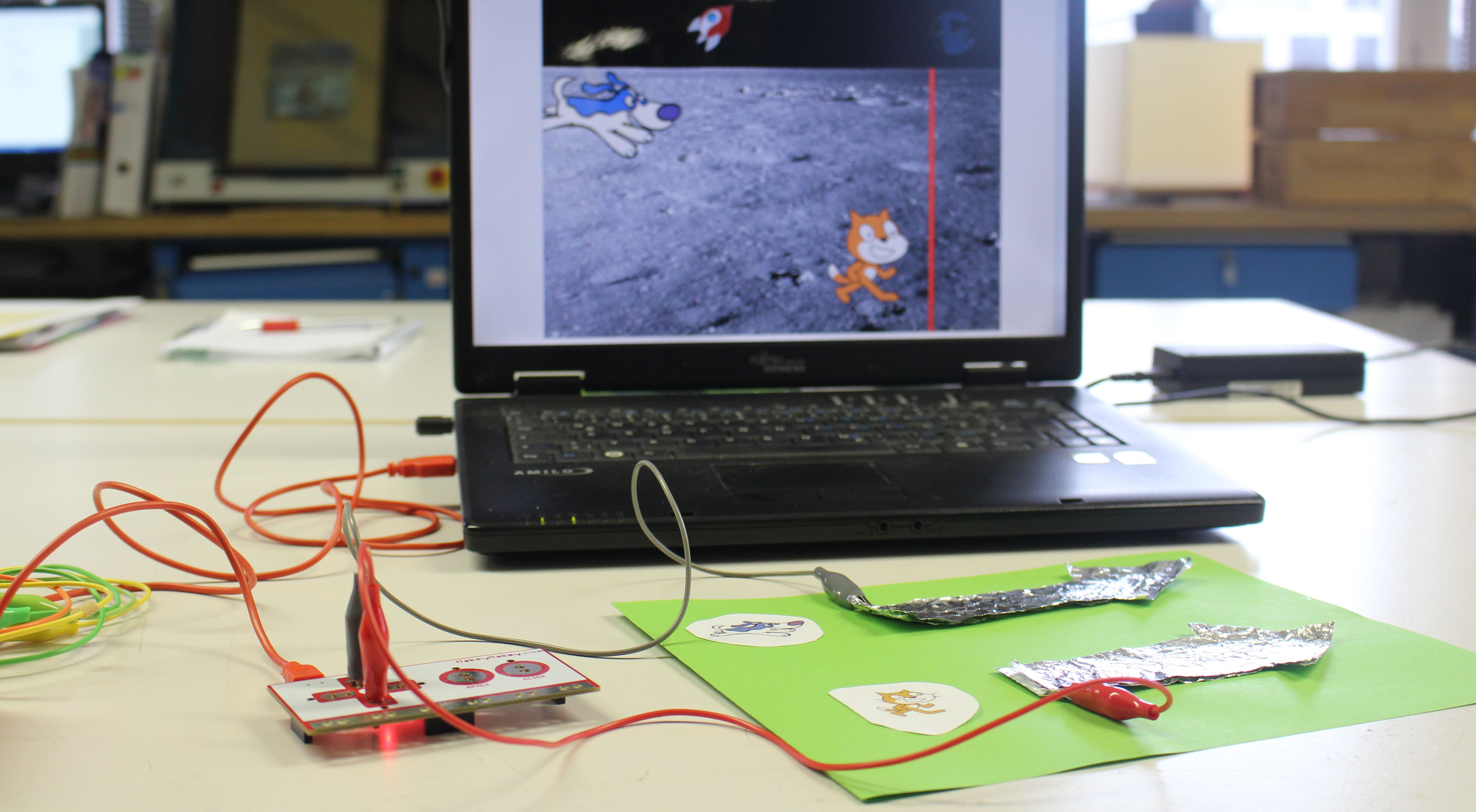 Laptop mit Scratch-programmierten Computerspiel mit selbstgebauten MaKey-MaKey-Controller: Zwei Pfeile aus Aluminiumfolie angeschlossen an die Steuerplatine