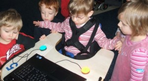 Kinder am Computer, ein Kind im Rollstuhl nutzt Taster, um den Computer zu bedienen