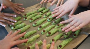Kinderhände mit unterschiedlichen Hautfarben über einem Backblech mit grünem Gebäck