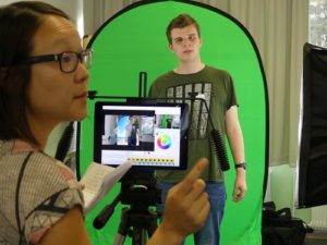 Junge Frau fotografiert mit Tablet auf Stativ Jugendlichen vor dem Greenscreen