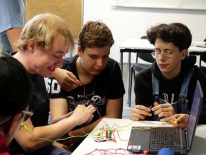 Jungen und Medientrainer vor Laptop, sie halten die Krokodilklemmen der MaKey MaKey Platine in den Händen