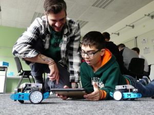 Johannes Rück erklärt einem auf den Boden liegenden Jungen, wie er mBot-Roboter mit der App mBlockly steuern kann