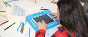 Mädchen vor iPad in blauer dicker Hülle und vielen bunten Stiften