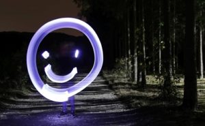 Lightpainting Foto: Ein lila-weißer Smiley, im Hintergrund dunkler Wald