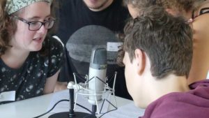Junge und Mädchen mit zwei Pädagogen vor einem Mikrofon