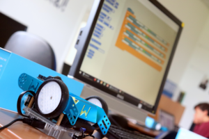 mBot Roboter vor Bildschirm mit Scratch-Programm