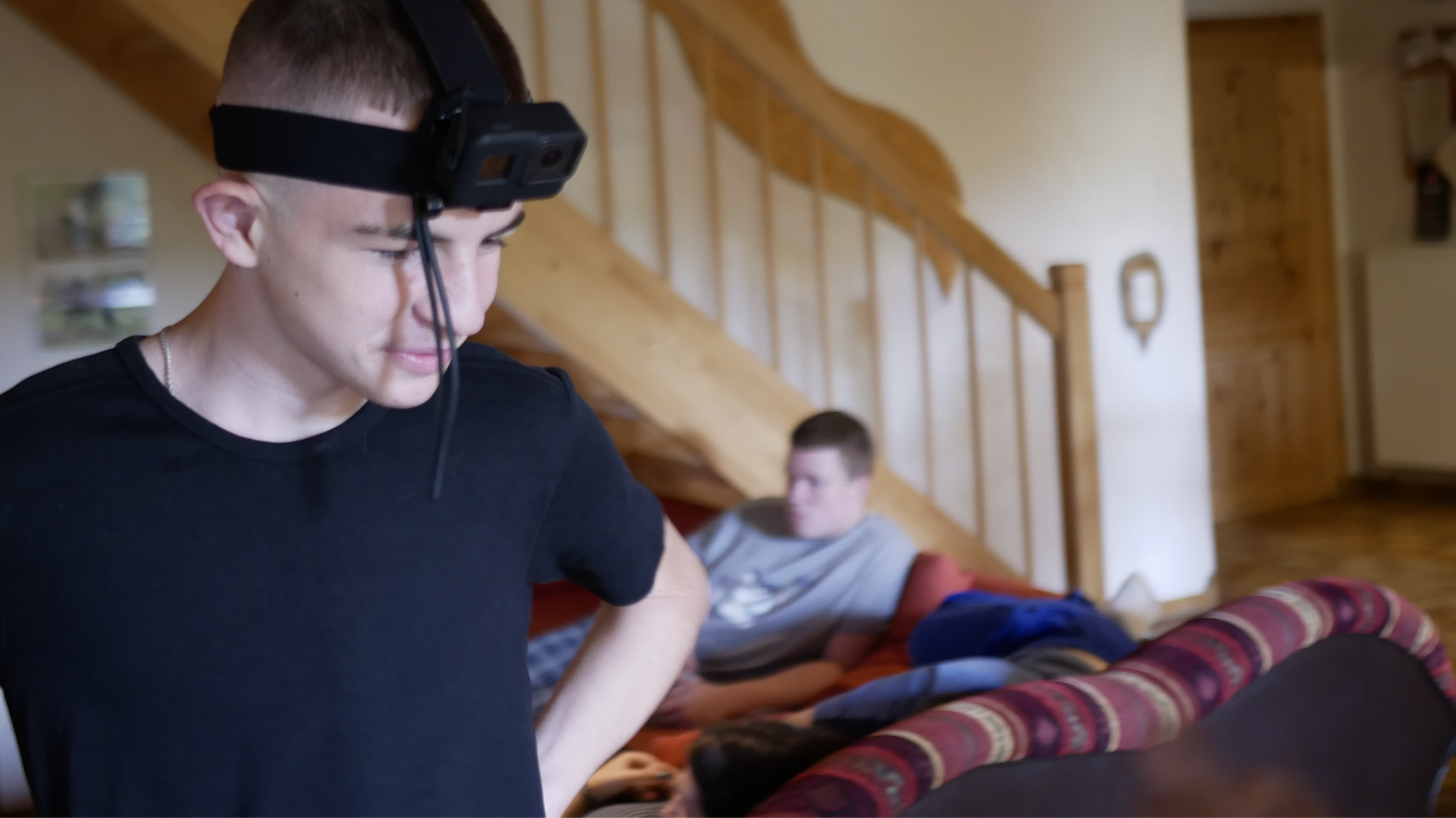 Ein Jugendlicher mit GoPro-Kopfhalterung im Vordergrund. Im Hintergrund ein weiterer Jugendlicher auf einem Sofa.