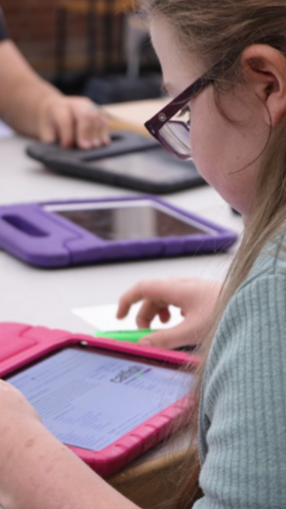 Jugendliche sitzt an einem Tisch mit vielen Tablets in bunten Hüllen