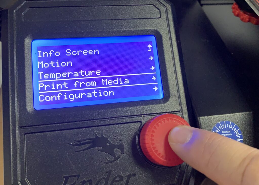 Ein Finger drückt auf einen roten Knopf. Der Bildschirm von dem schwarzen Gerät sagt "Print from Media"