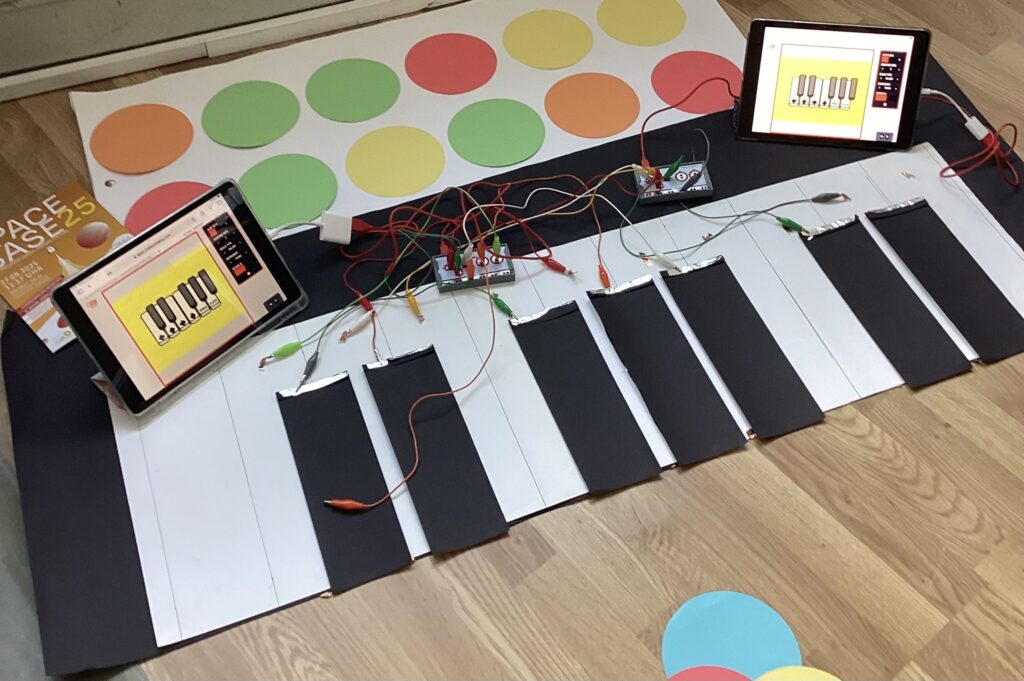 Ein Klavier scheinbar aus einem dünnen Material auf dem Boden, angeschlossen an viele bunte Kabel