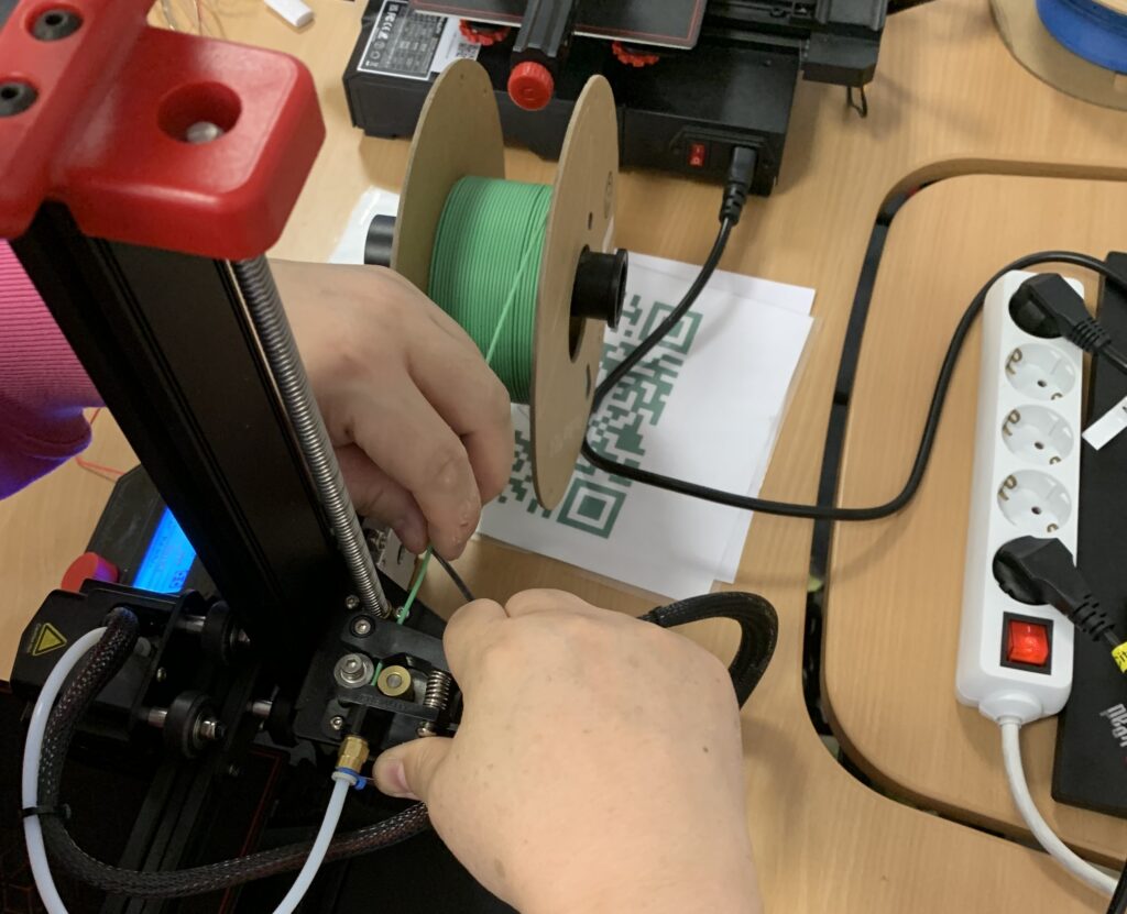 Zwei Hände setzen grünes Filament (das Druckmaterial) in einen 3D-Drucker ein.