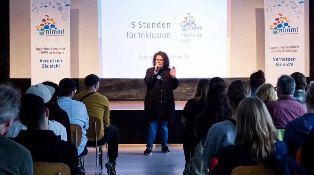 Die Referentin steht vor einem großen Publikum und scheint eindringlich etwas zu erläutern.