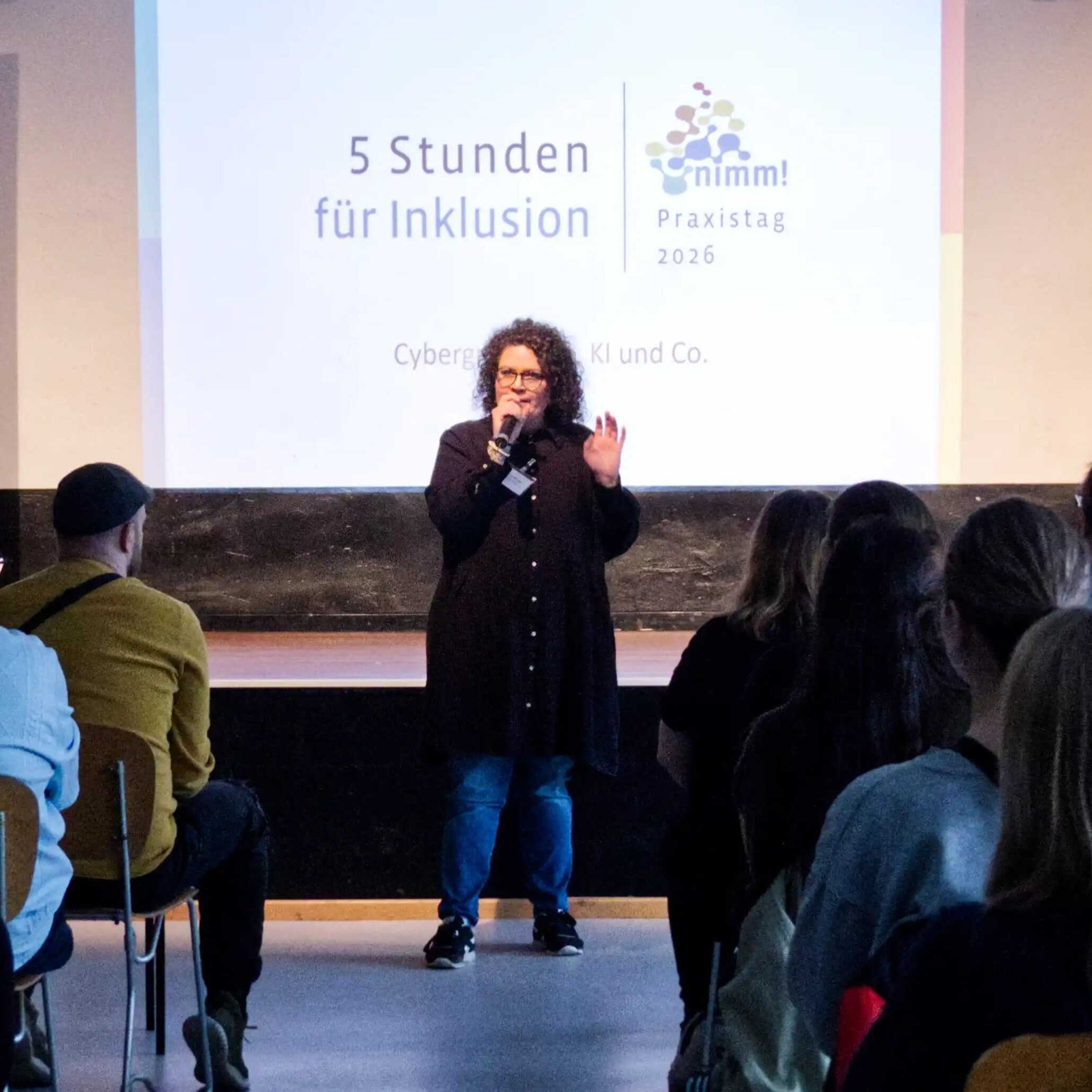 Die Referentin steht vor einem großen Publikum und scheint eindringlich etwas zu erläutern.